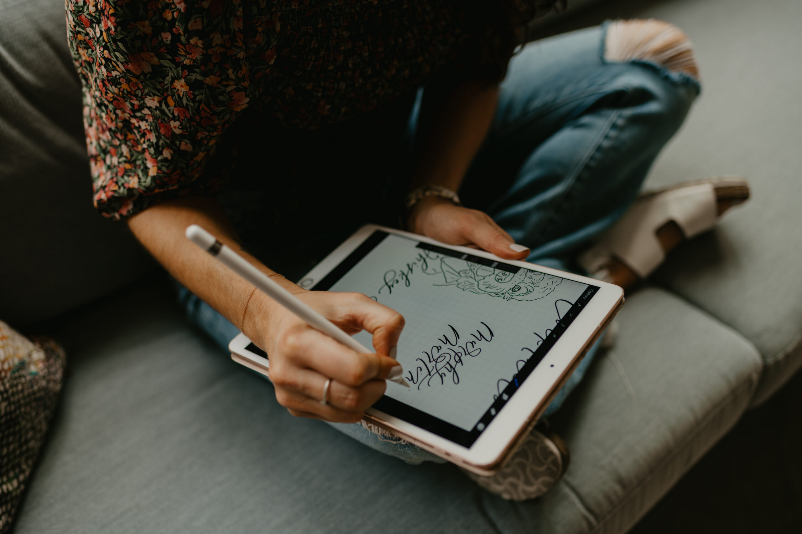 A person sitting at a desk with a laptop open, practicing calligraphy on paper with a brush pen, showing how to teach yourself calligraphy at home.