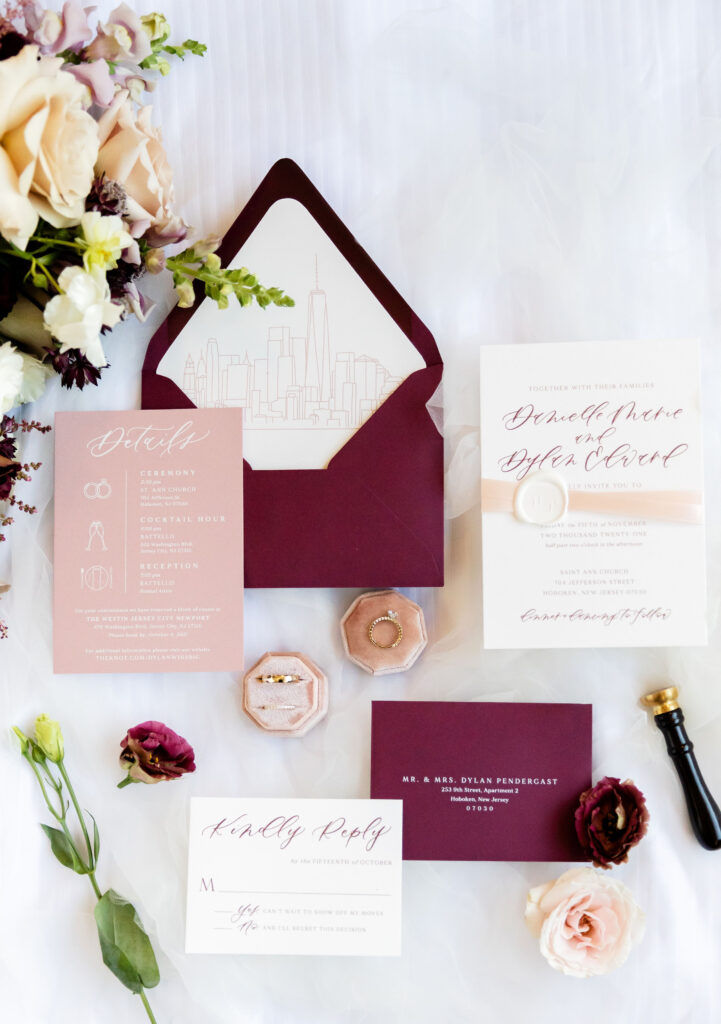 Modern wedding flat lay with burgundy stationery, gold rings, floral accents, and New York skyline liner. Calligraphy business from scratch