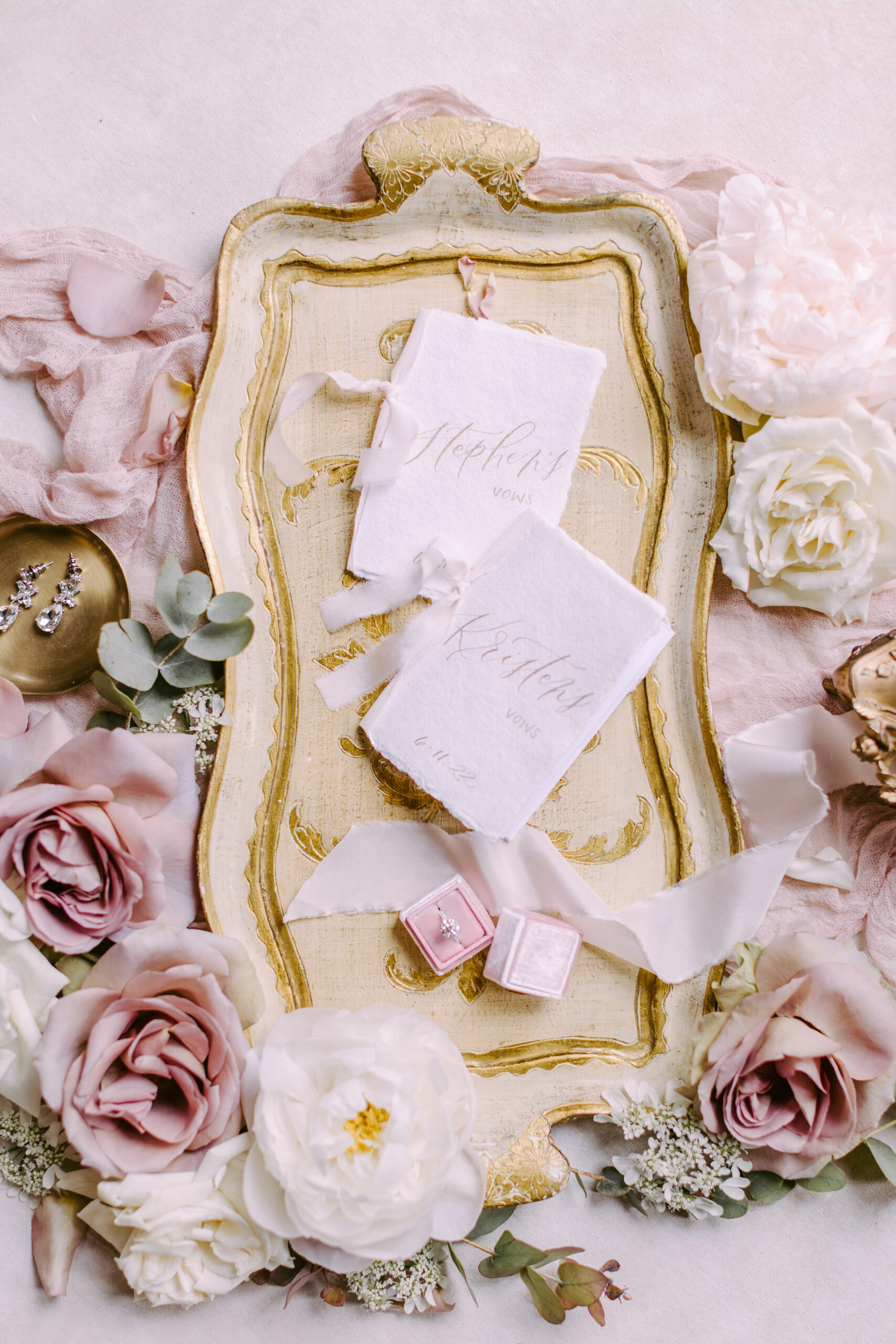 Romantic flat lay featuring vow booklets, roses, vintage tray, pink ring box, and delicate accessories - calligraphy business from scratch