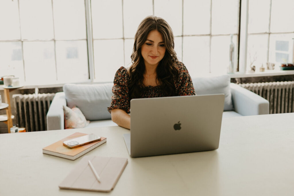 Woman working on a laptop at a bright, modern desk, creating content about marketing tips for calligraphers and invitation designers.