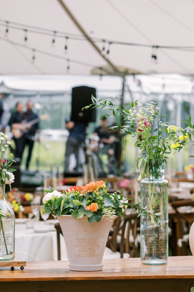 Creative wedding seating chart display using hand-lettered calligraphy on flower pots and glass bottles — unique marketing tips for calligraphers.