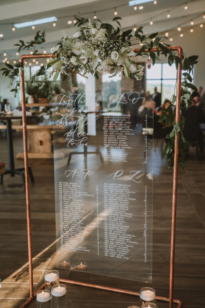 Clear acrylic wedding seating chart with white calligraphy. A great visual for content about should you start a podcast for your wedding business.