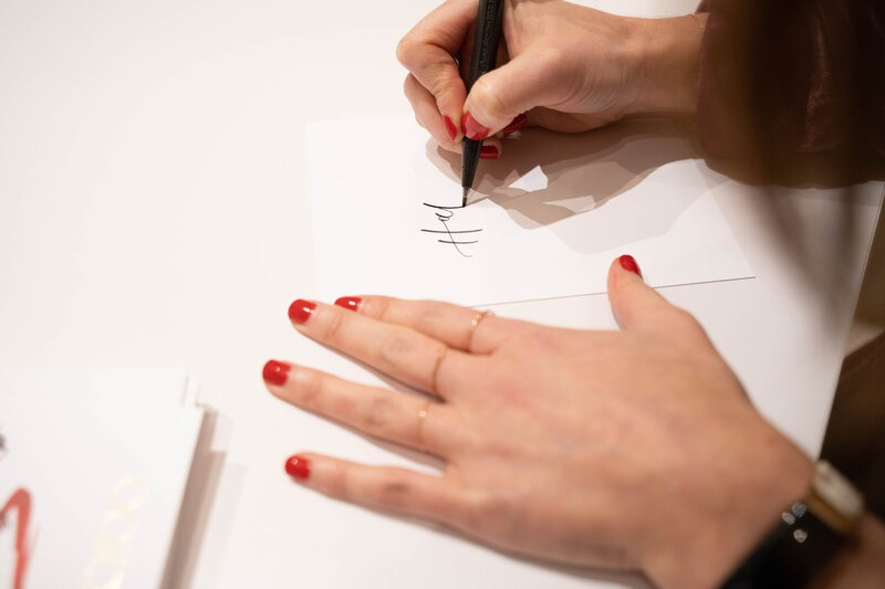 Close-up of a stationer hand lettering on white card, illustrating pricing strategies for stationers through custom work.