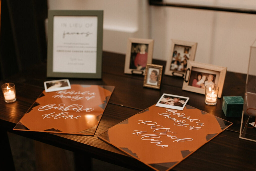 Memorial table with framed photos, candles, and custom acrylic signs honoring loved ones at a wedding.